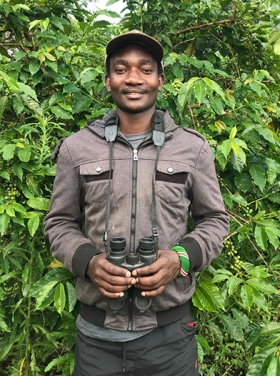 Frank Juma Ong’ondo standing in front of a tree with binoculars in his hands